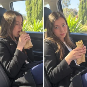 Charlotte Walker seated in a car holding and eating a sausage roll.